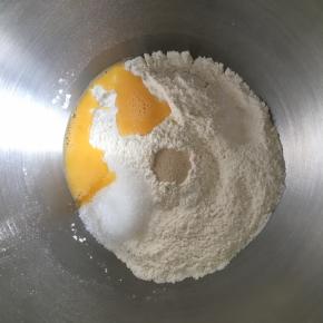 盆哪倒入高筋面粉和低筋面粉，混合均匀，中间挖一小孔，倒入活性干酵母，盐和糖对角线放置，倒入全蛋液