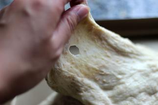 伸拉面团，有光滑的破洞形成，代表面团已揉好，盖保鲜膜发酵待面团涨至2倍大