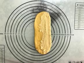 取一面团，擀成长舌形，四周拍出空气。
翻面后一侧抹上椰蓉馅。