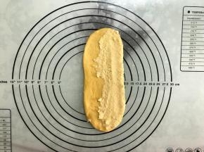 取一面团，擀成长舌形，四周拍出空气。
翻面后一侧抹上椰蓉馅。