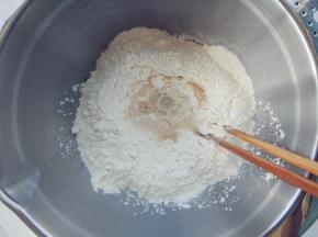 将福临门麦芯高筋雪花粉倒入面盆中，在中间挖一个坑，倒入酵母粉后，逐次少量倒入冷水，用筷子拌成雪花状