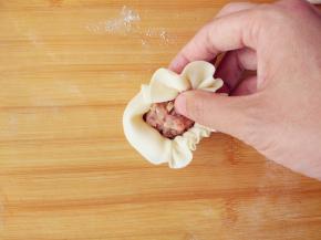 用勺子将适量馅料放在面片中心，左手托底，在右手捏褶的同时，慢慢转动，且用左手拇指将馅料不断向内压，这样可以包入更多馅料。右手用拇指食指不断将面片边缘均匀折叠，用剩余几指在边缘下方压实。距离边缘越远，花瓣越大，反之则越小