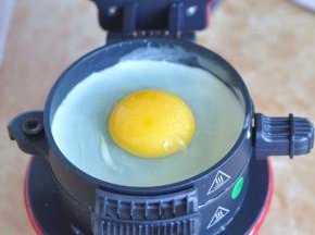 将早餐机上层的组件放下，先刷一层油，再打入鸡蛋，表面撒一点盐，盖上上面盖子，持续加热让鸡蛋凝固。