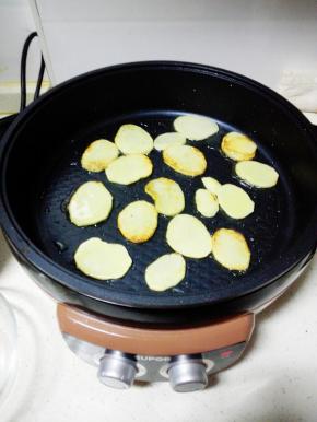 煎烤机内放入一大勺玉米油，中火烧热后，放入土豆片，煎至两面金黄色，出锅备用