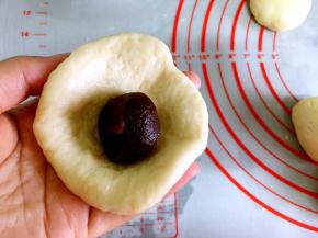 取一个小面团用手轻轻按圆，中间包入一个豆沙球，用包包子的手法包起来，褶皱处在下面，搓圆。