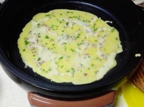 煎烤机中大火，倒入一半的培根鸡蛋糊，用锅铲抹成薄薄的一层