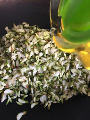 3.将槐花放在锅内，倒入玉米油拌均匀；