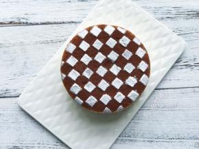 蛋糕表面撒上一层可可粉，垫上印花筛，撒上糖粉做成棋盘图案。