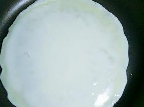 倒入适量鸡蛋面糊，立刻转动锅子，让面糊均匀摊开，等面糊表面凝固