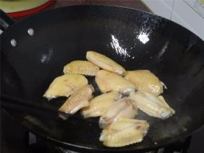 锅里下油，大火烧热后加入鸡翅，煎香。加入几片姜片到鸡翅上。