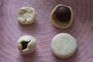 取一个面团，两头对折，用手捏成圆形如图，包入馅料，用虎口捏紧收口。按扁即成月饼。