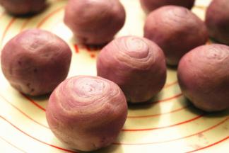 擀好的面皮，翻过来，包上一颗紫薯蛋黄，继续虎口法收圆，收口向下，顶部可以看到隐约的层次。