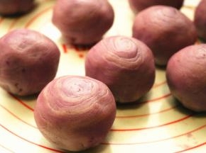 擀好的面皮，翻过来，包上一颗紫薯蛋黄，继续虎口法收圆，收口向下，顶部可以看到隐约的层次。