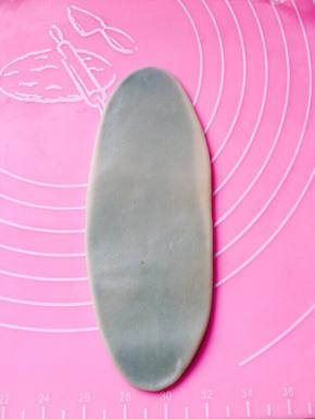 将包裹好的面团擀成牛舌型，从上往下卷成卷