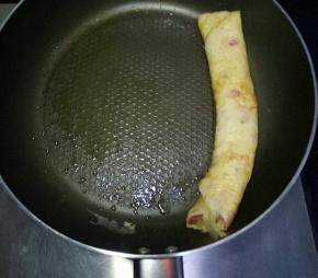 中小火等待鸡蛋液表面半凝固时，用筷子和铲子配合从右往左卷起来推到一边