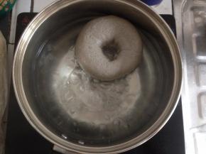 将煮贝果用的50克糖放进装了1000克水的锅里，煮开。提起油纸，将贝果放入到锅里，两面各煮20秒。用筛网将贝果捞起，沥干水分，摆放在烤盘上。