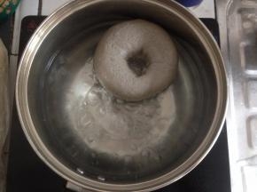 将煮贝果用的50克糖放进装了1000克水的锅里，煮开。提起油纸，将贝果放入到锅里，两面各煮20秒。用筛网将贝果捞起，沥干水分，摆放在烤盘上。