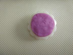 取一个彩色面团，分割成两份，每个5克，揉成圆形，轻轻的按压在月饼模具的花片上，力度要均匀分布。（每种彩色面团是10克，每种颜色可以印出两个月饼）