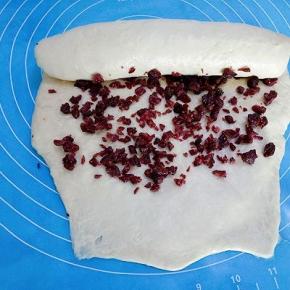 在面团表面撒些蔓越莓碎，由上往下卷起