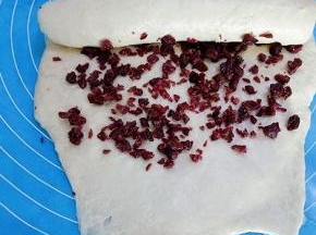 在面团表面撒些蔓越莓碎，由上往下卷起