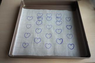 取一张油纸，打好格子，在上面画上心形图案，然后铺在烤盘内
