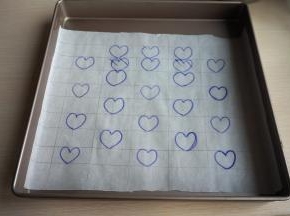 取一张油纸，打好格子，在上面画上心形图案，然后铺在烤盘内
