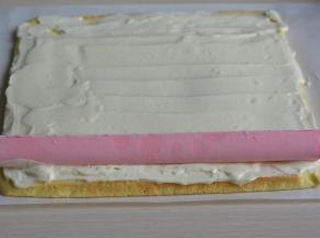 将奶油奶酪糊均匀地抹在蛋糕片上，开始的部位可以厚一点，结尾的部位抹薄薄的一层；将冻好的粉色奶酪夹心从模具中取出，速度要快噢；取合适的长度铺在蛋糕片的一端；从下向上卷起，然后用油纸包裹好，再略微用力按一下，使夹心能紧密贴合