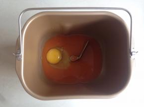 将胡萝卜汁和鸡蛋加入到面包桶内。