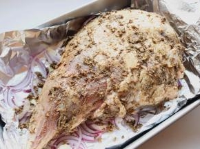 刚才混合好的调料均匀抹在腌过的羊腿上，全身都抹匀，放在烤盘内洋葱上面。