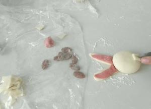 如图这样，做出耳朵，黑色面团整成椭圆形。然后切一块面团做门牙。