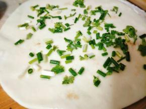 然后擀成一张圆饼，倒入少许食用油，撒上葱花、少许的盐和调料，均匀抹开；