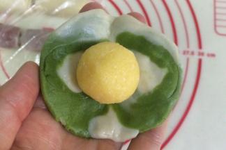 然后把面团按扁压平，也可以利用擀面杖擀开，中间厚四周薄，包入一份椰蓉馅。