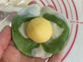 然后把面团按扁压平，也可以利用擀面杖擀开，中间厚四周薄，包入一份椰蓉馅。