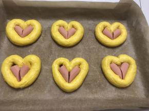 10 把搓长的的面团在烤盘里摆成心形，中间放入切好的火腿肠，全部做完六个