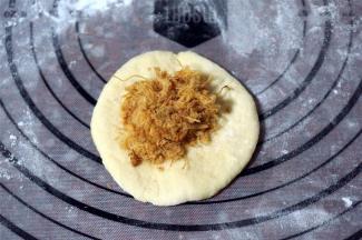 取一份面团，揉圆后压扁，放入肉松，包好，收口朝下。