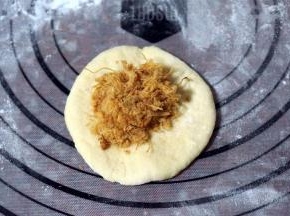 取一份面团，揉圆后压扁，放入肉松，包好，收口朝下。