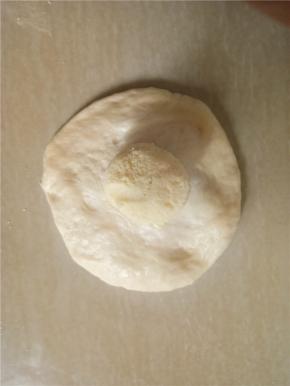 取一小面团擀成边缘薄中间厚的面片，包入奶酥。收紧收口。