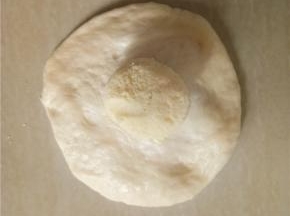 取一小面团擀成边缘薄中间厚的面片，包入奶酥。收紧收口。