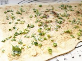 分成两份，先取一份擀成大一点的长方形面片，抹上刚才我做好的花生酱，淋上一些花生油，撒盐以及五香粉，再撒上切碎的葱末，然后卷起来。