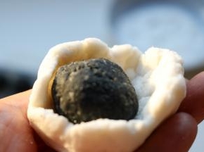 糯米面团按扁，包入冻硬的黑芝麻陷，收紧收口。