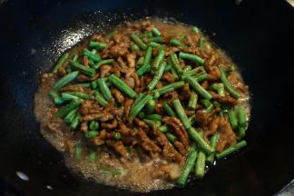 5.将豇豆倒入锅中，翻炒均匀后，倒入热水，与菜料持平即可，转小火，焖几分钟；