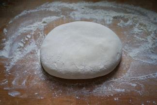 5.饧好的面团放在案板上，撒少许面粉揉成光滑状再用手掌按扁；