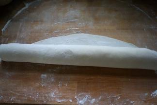 8.擀面杖从底边向上卷起，一边卷一边压，使面片变得越来越薄、越来越大；可把四边都分别这样重复几次；