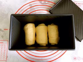 取一个面团擀成长椭圆形，左右边对折，底边压薄，从上往下卷起。其他两个面团也依次卷好。放在学厨吐司盒中。