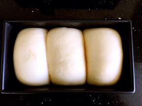 烤箱底部放碗热水，再把吐司盒用保鲜膜包裹好放在烤箱中进行二发至八分满，盖上吐司盒的盖子。