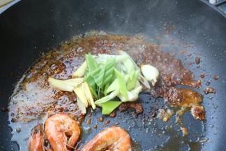 把虾推到一边，下入麻辣香锅底料继续炒。炒香麻辣香锅底料后，下入葱姜蒜继续炒出香味来。