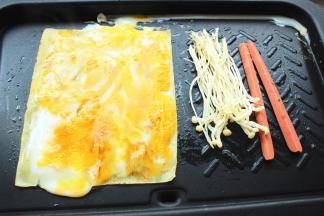 用铲子把鸡蛋均匀抹在冷面上，同时在边上煎香香肠和金针菇。