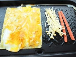 用铲子把鸡蛋均匀抹在冷面上，同时在边上煎香香肠和金针菇。