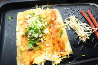 借助铲子把冷面翻面，再次喷一些水，淋上一些醋，我是直接把醋和水混合，一起刷上去，这一面也刷一些酱，撒一些香菜末和葱末，以及洋葱末。