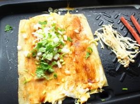 借助铲子把冷面翻面，再次喷一些水，淋上一些醋，我是直接把醋和水混合，一起刷上去，这一面也刷一些酱，撒一些香菜末和葱末，以及洋葱末。